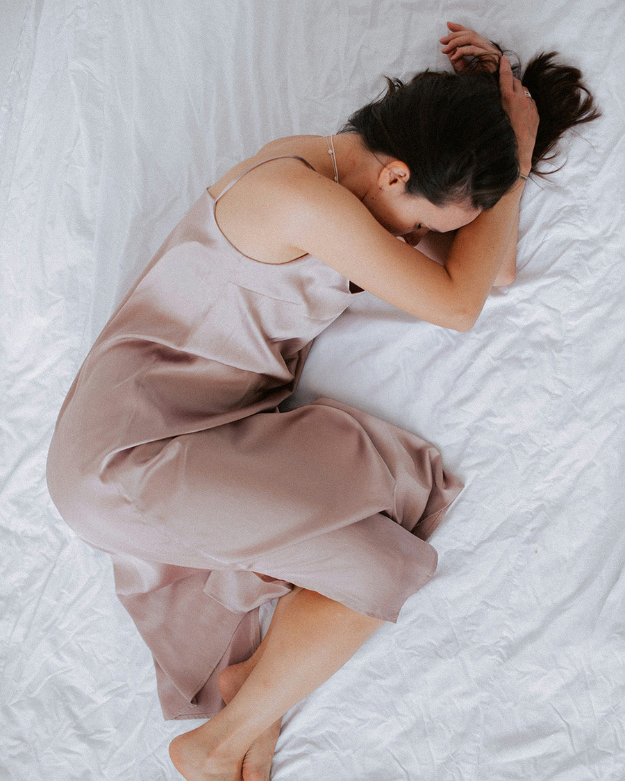 A woman curled up asleep on white bedding