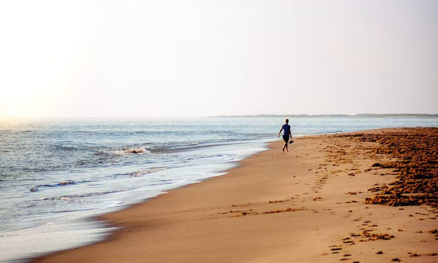 A woman walking along the beach in the early morning sun.