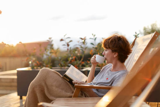 A woman relaxing on a deck chair at sunset with a book and a cup of tea.