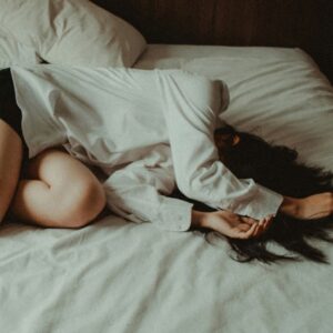 A woman lying awake on her bed with her arm over her face
